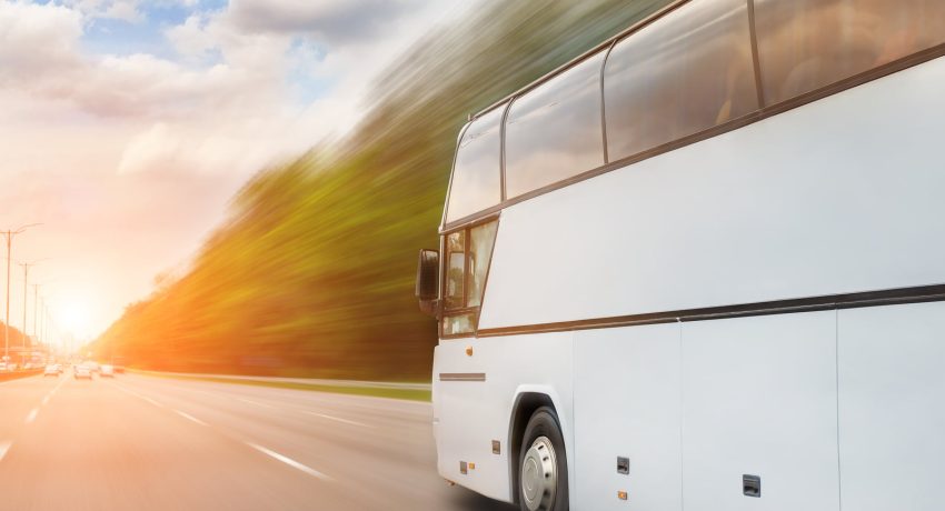 Big luxury comfortable tourist bus driving through highway on bright sunny day. Blurred motion road. Travel and coach tourism concept. Trip and journey by vehicle